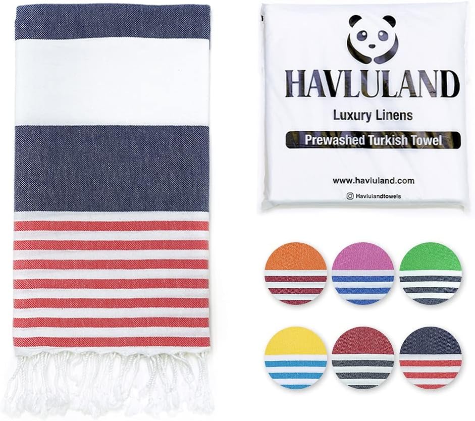 Havluland Turkish towel in navy and red stripes with white fringe, shown unfolded beside its white branded packaging. Six circular color variant swatches are displayed, showing orange, purple, green, yellow, burgundy, and navy stripe options.