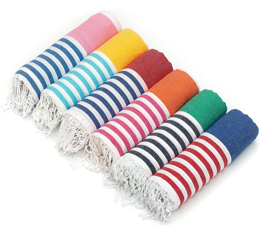 Six rolled Turkish cotton towels fanned out on a white background, each with navy blue and white stripes on one end and a solid color on the other: pink, teal, yellow, orange, red, and green. White fringe tassels visible on left ends.